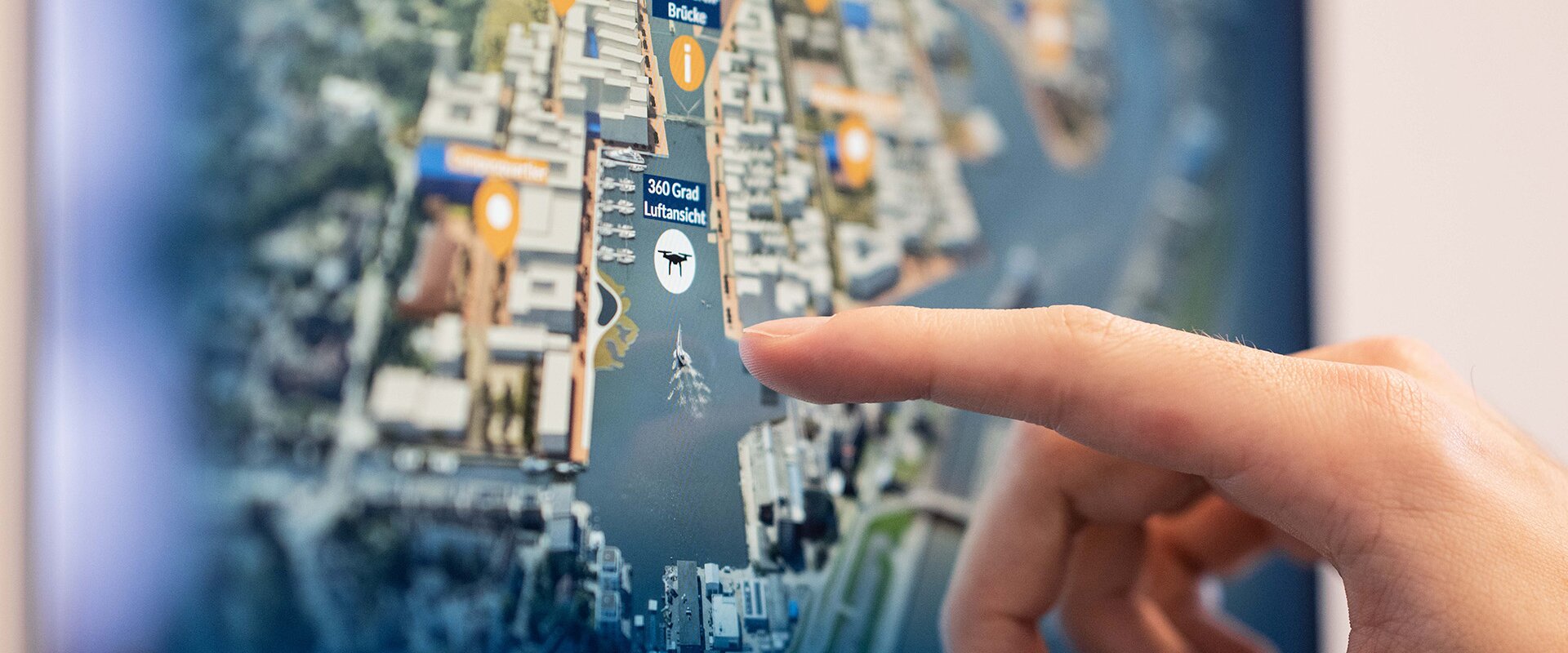Die interaktive 3D-Anwendung zeigt das Werftquartier Bremerhaven als zukünftiges Stadtquartier im räumlichen Kontext, ein Finger schwebt über der Anwendung über einen der Marker der einzelnen Nachbarschaften. 
