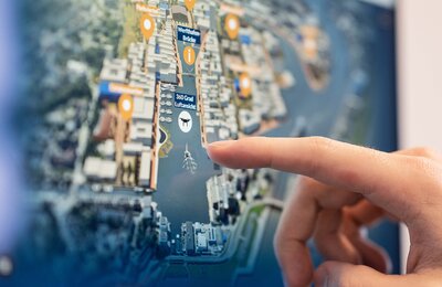 Die interaktive 3D-Anwendung zeigt das Werftquartier Bremerhaven als zukünftiges Stadtquartier im räumlichen Kontext, ein Finger schwebt über der Anwendung über einen der Marker der einzelnen Nachbarschaften. 